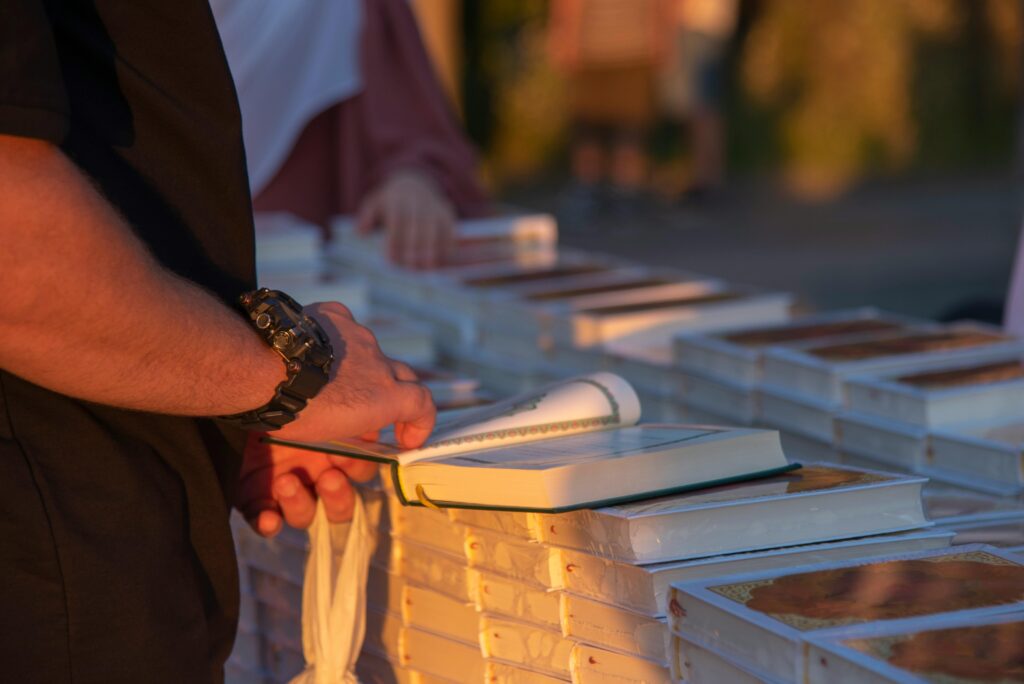 A person flipping through books at an outdoor market stall during sunset.